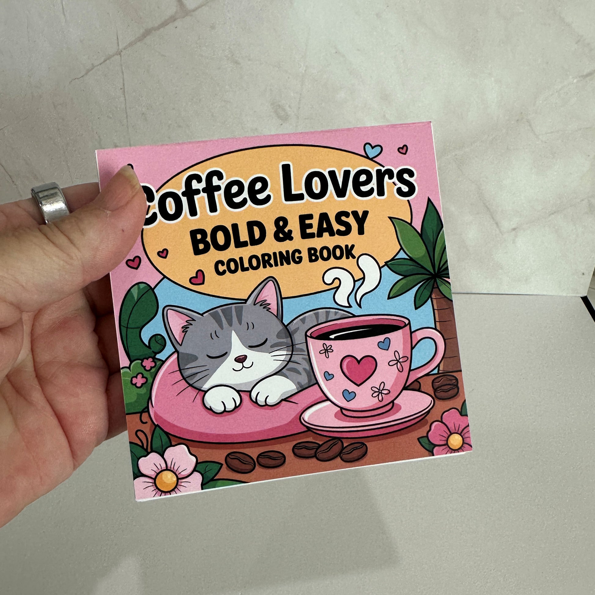 Coffee Lovers Bold and Easy Mini Coloring Book featuring cute sleeping kitten beside a pink coffee cup with cozy café themed illustrations.