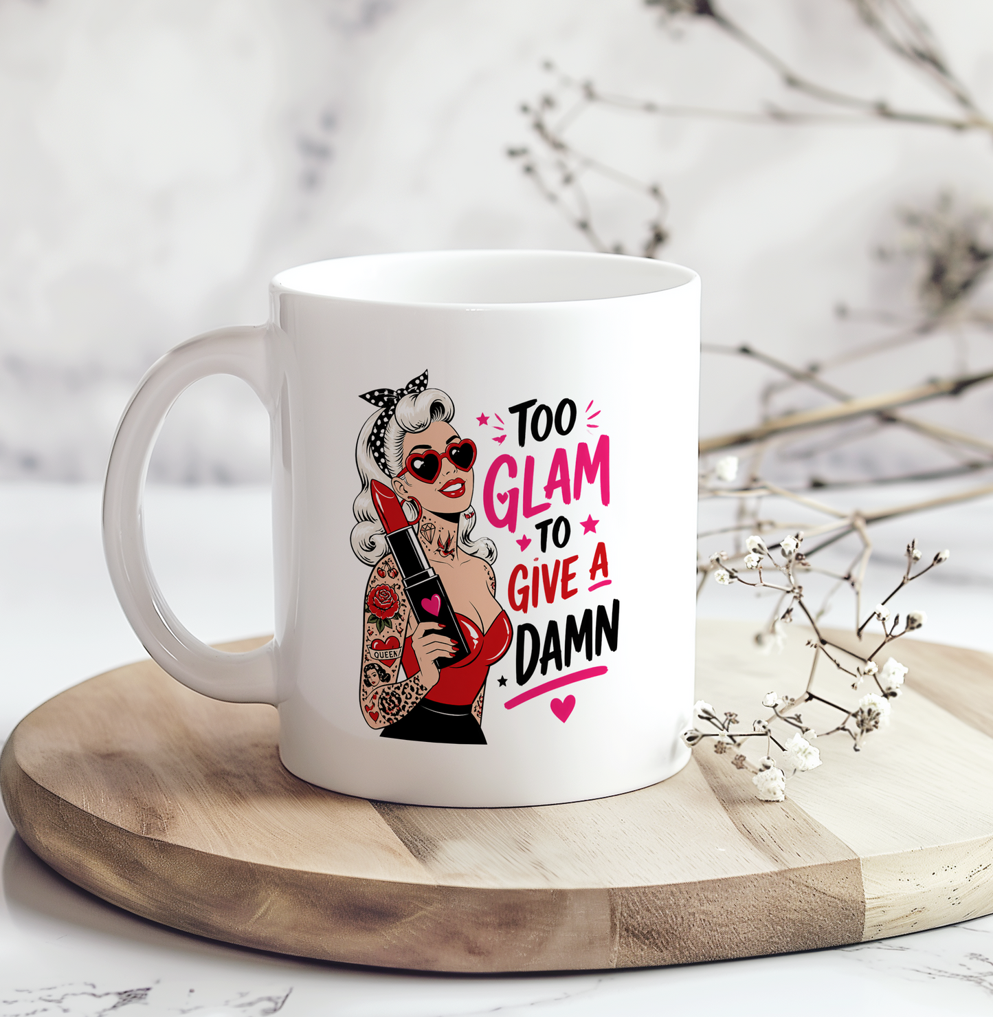 White ceramic mug featuring a retro tattooed pin-up woman wearing heart-shaped sunglasses and holding lipstick beside the phrase "Too Glam To Give A Damn."