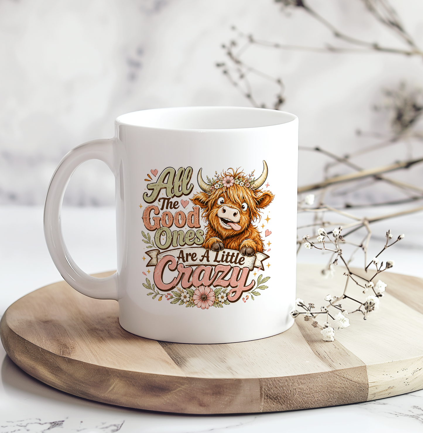 White ceramic mug featuring a cute Highland cow with flowers and the funny quote "All the Good Ones Are a Little Crazy" in rustic farmhouse colors.
