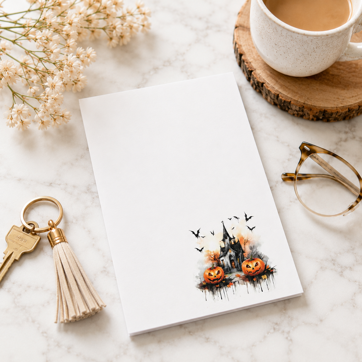 White Halloween notepad featuring a haunted house, smiling pumpkins, bats, and autumn accents in the lower corner.