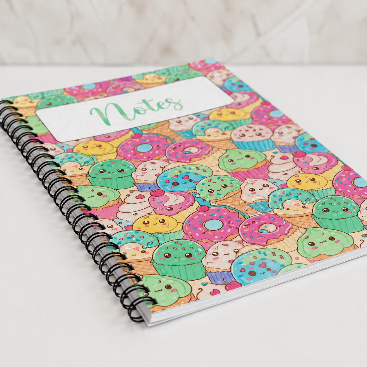 Pastel kawaii dessert spiral notebook featuring cute donuts, cupcakes, ice cream treats, and smiling sweets on a colorful glossy cover.