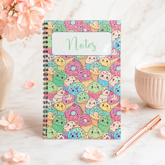 Pastel kawaii dessert spiral notebook featuring cute donuts, cupcakes, ice cream treats, and smiling sweets on a colorful glossy cover.