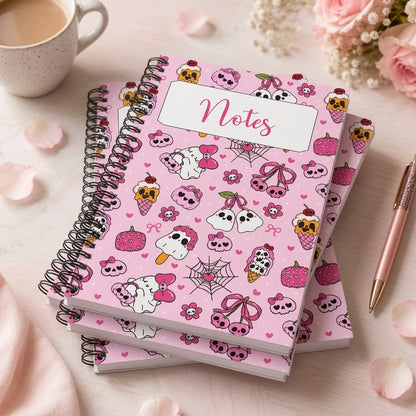 Pink spiral notebook featuring kawaii ghosts, skulls, bows, hearts, strawberries, and spooky sweet illustrations on a pastel pink background with a Notes label on the cover.