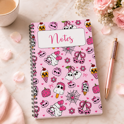 Pink spiral notebook featuring kawaii ghosts, skulls, bows, hearts, strawberries, and spooky sweet illustrations on a pastel pink background with a Notes label on the cover.