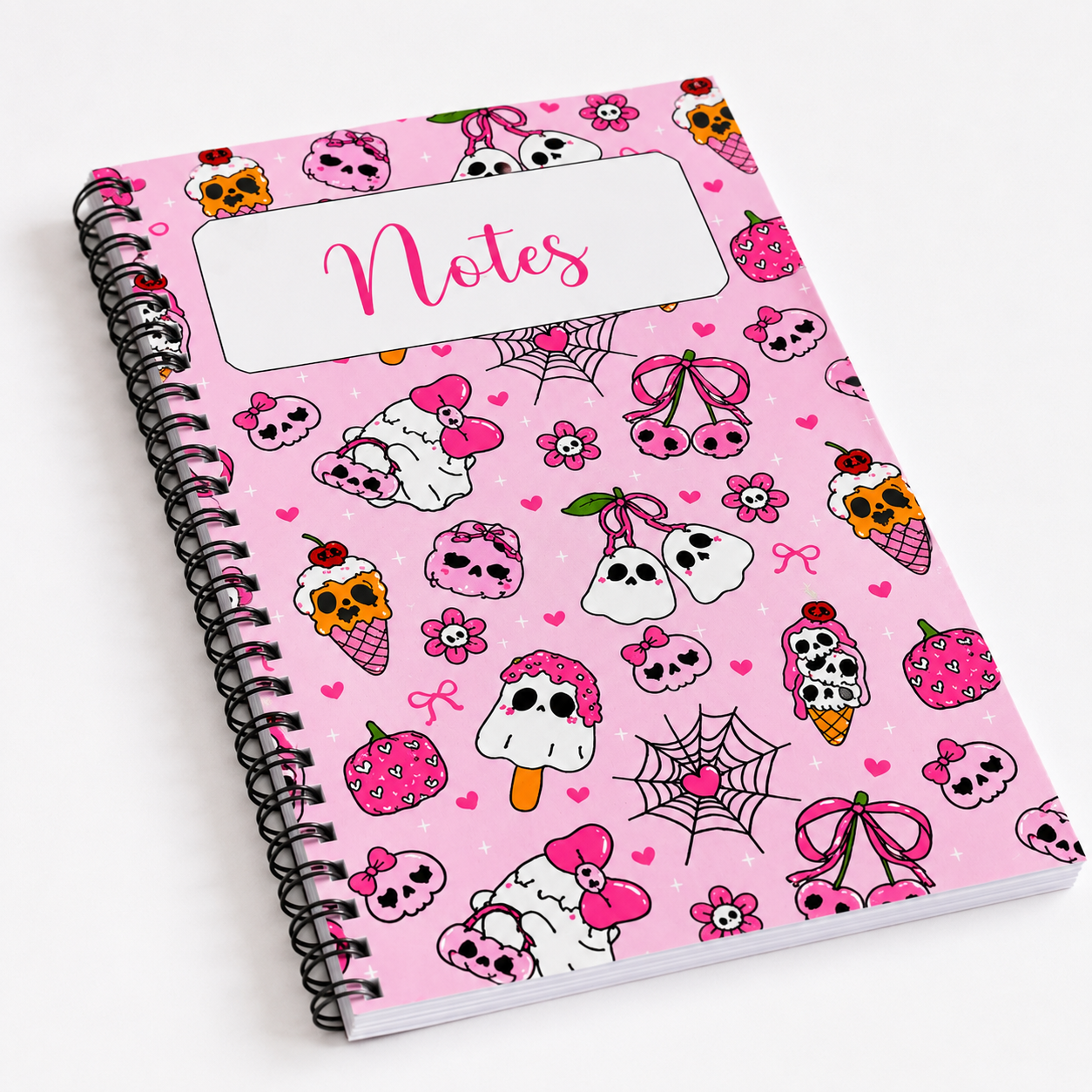 Pink spiral notebook featuring kawaii ghosts, skulls, bows, hearts, strawberries, and spooky sweet illustrations on a pastel pink background with a Notes label on the cover.