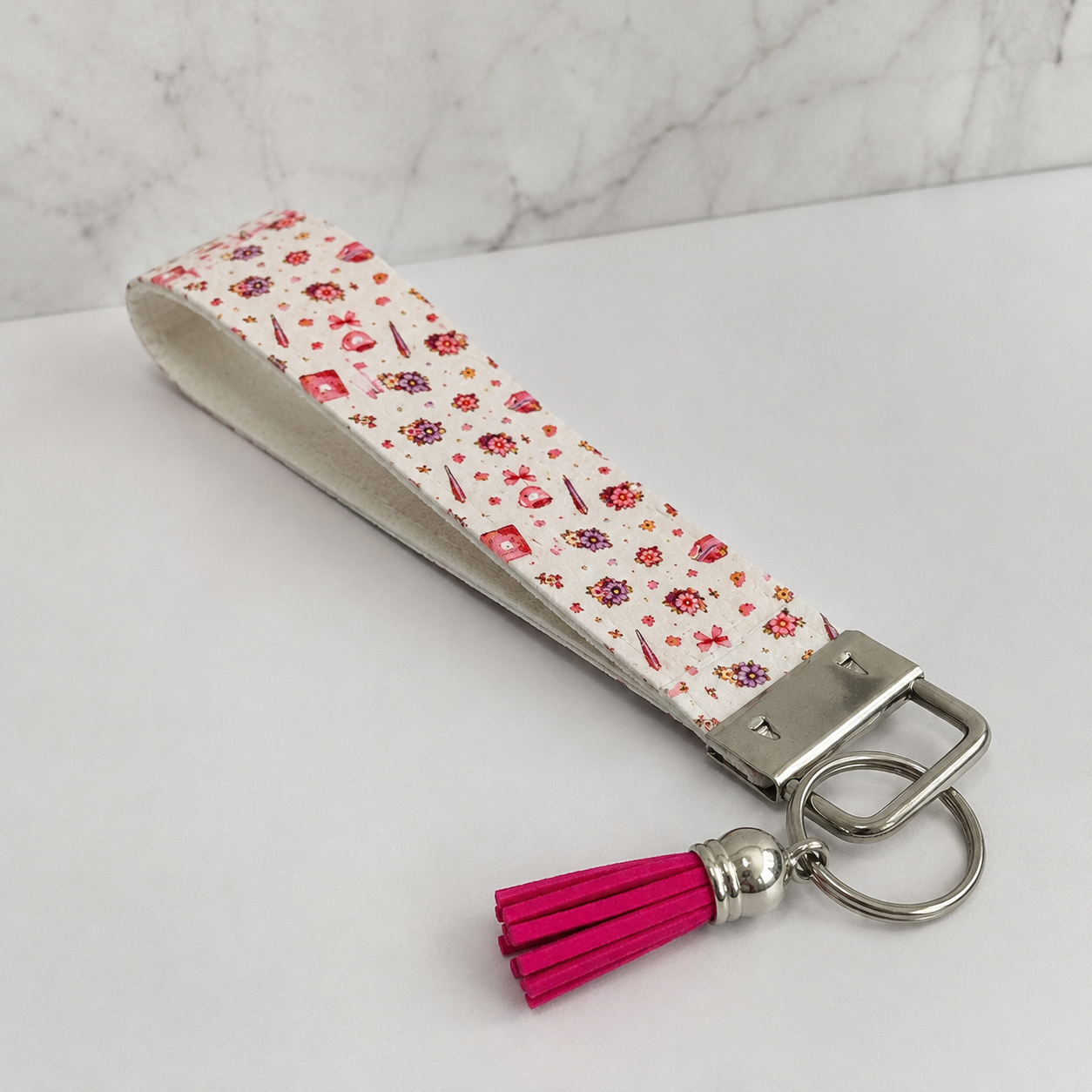 Pink floral fabric wristlet keychain with silver hardware and bright pink tassel displayed on a neutral background.