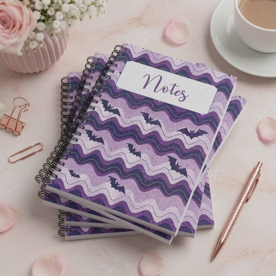 Purple spiral-bound notebook featuring whimsical bat artwork and wavy lavender patterns, perfect for notes, journaling, planning, and everyday writing.