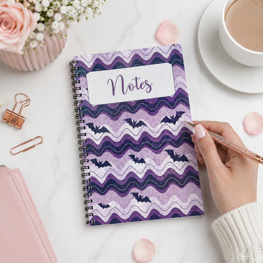 Purple spiral-bound notebook featuring whimsical bat artwork and wavy lavender patterns, perfect for notes, journaling, planning, and everyday writing.