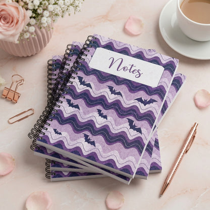 Purple spiral-bound notebook featuring whimsical bat artwork and wavy lavender patterns, perfect for notes, journaling, planning, and everyday writing.