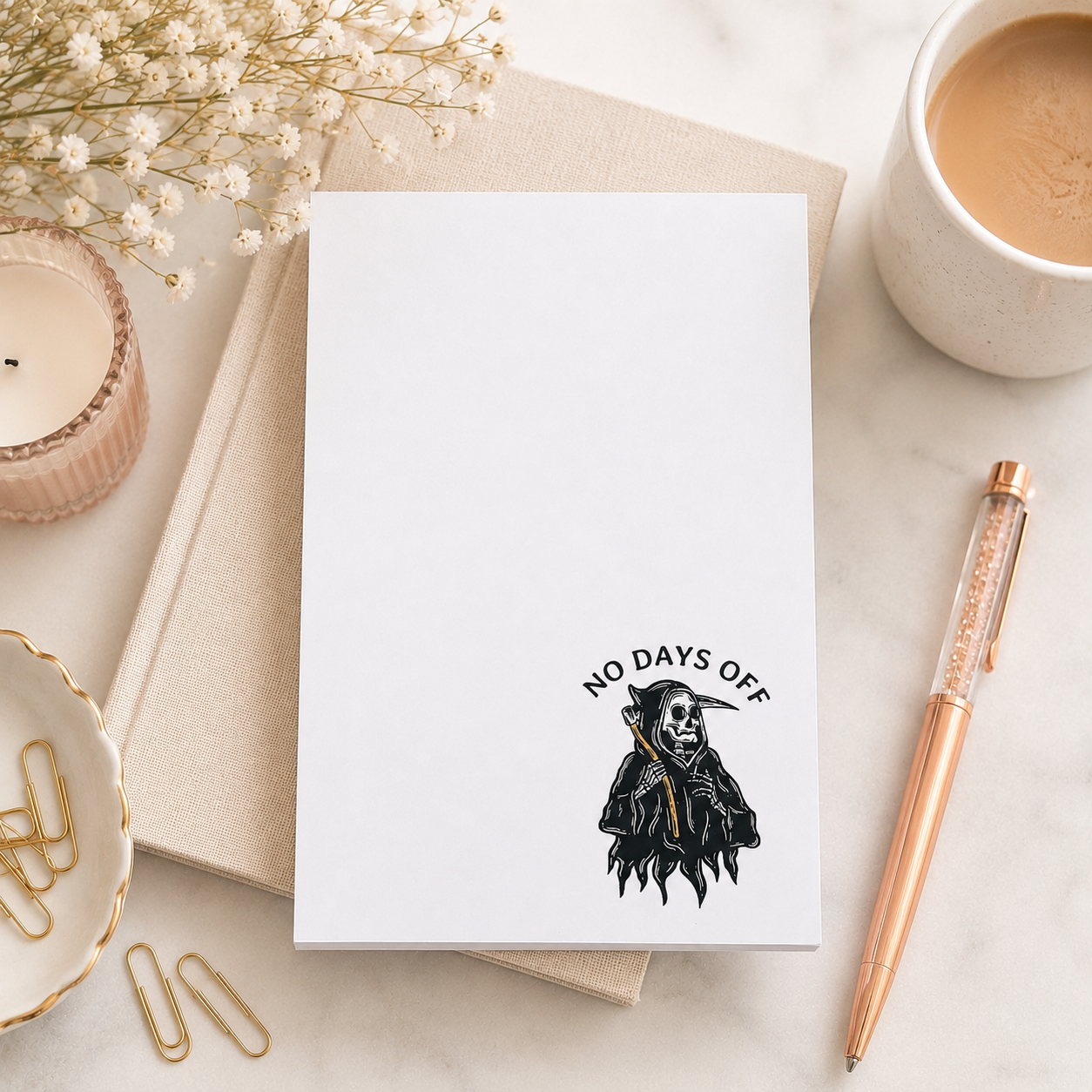 White notepad featuring a small grim reaper illustration and the words "No Days Off" in a minimalist dark humor design for notes, lists, and reminders.