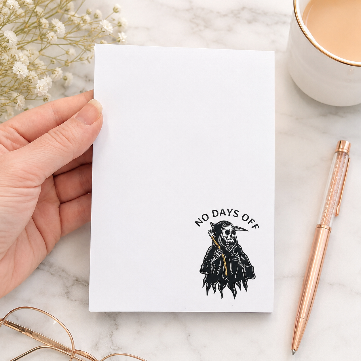 White notepad featuring a small grim reaper illustration and the words "No Days Off" in a minimalist dark humor design for notes, lists, and reminders.
